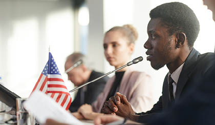 Side view of African businessman performing during conference he sitting at the table and speaking into the microphone